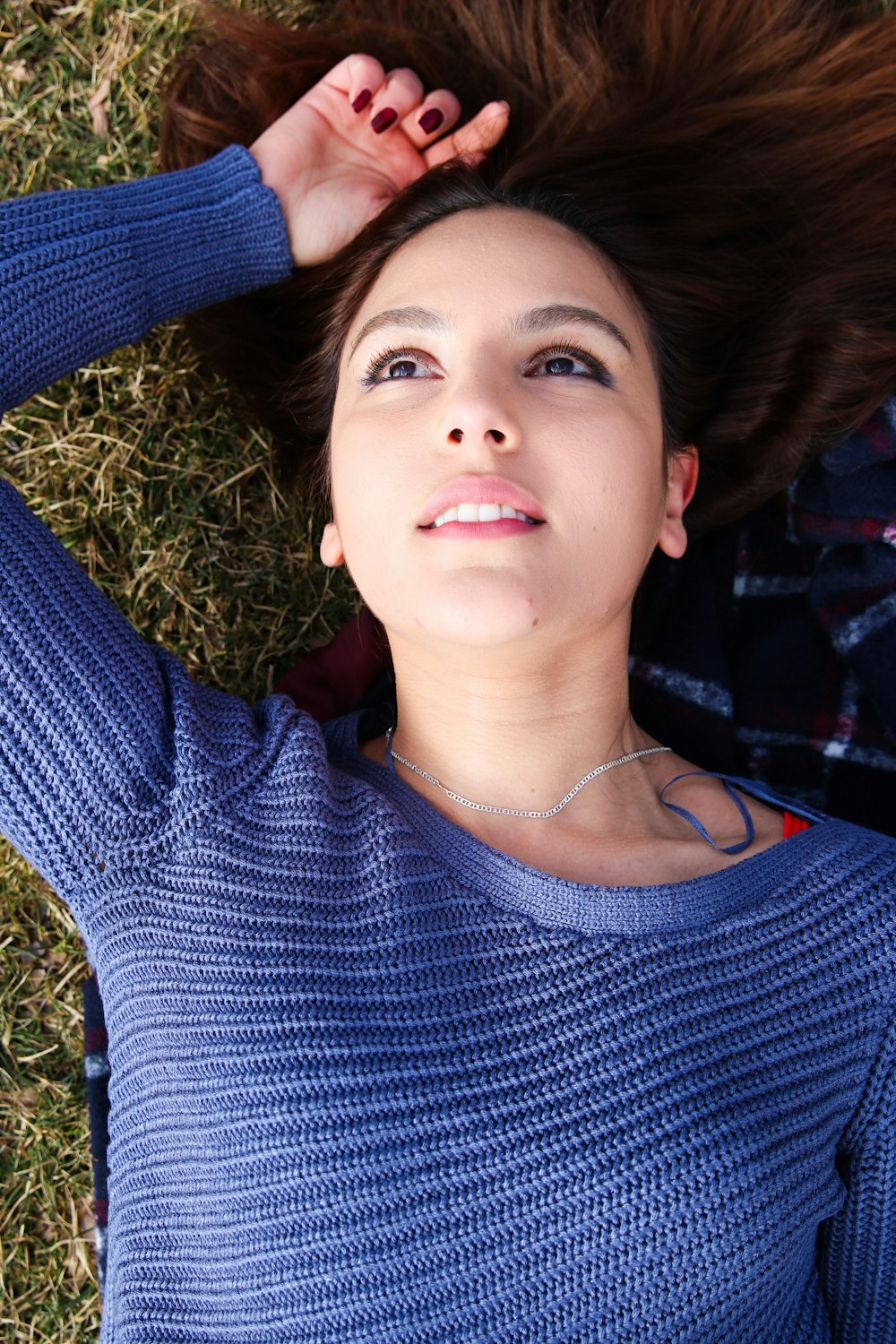 Femme en chemise à manches longues à col rond bleu et noir couchée sur l’herbe verte pendant la journée