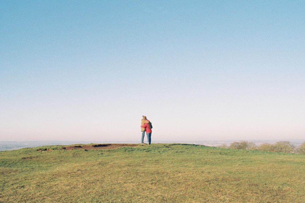 woman in pink jacket standing on green grass field under blue sky during daytime