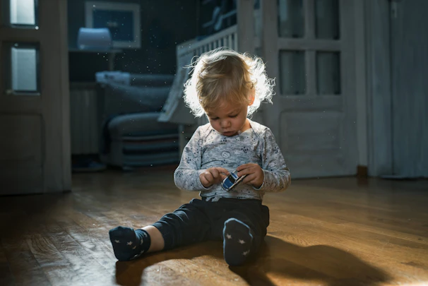 Smiling child holding a handcrafted wooden toy car with natural light streaming through a window.