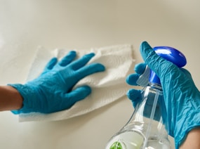 person holding blue textile near clear glass bottle