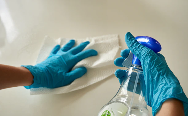 Hands in blue nitrile gloves wiping a white surface with a paper towel