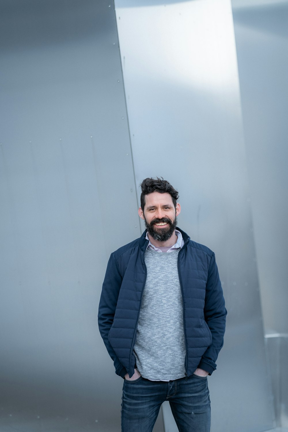 man in blue jacket standing near white wall