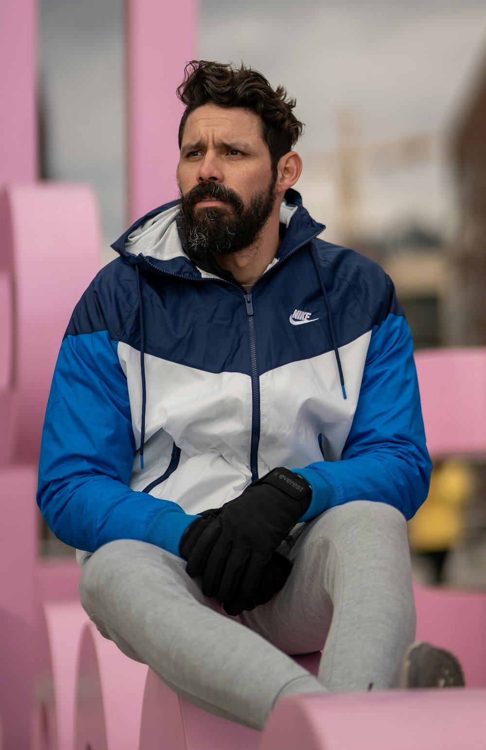 man in blue and white zip up jacket and gray pants sitting on brown wooden bench