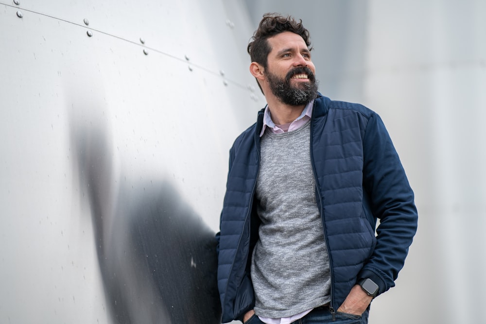 man in blue zip up jacket standing beside white wall