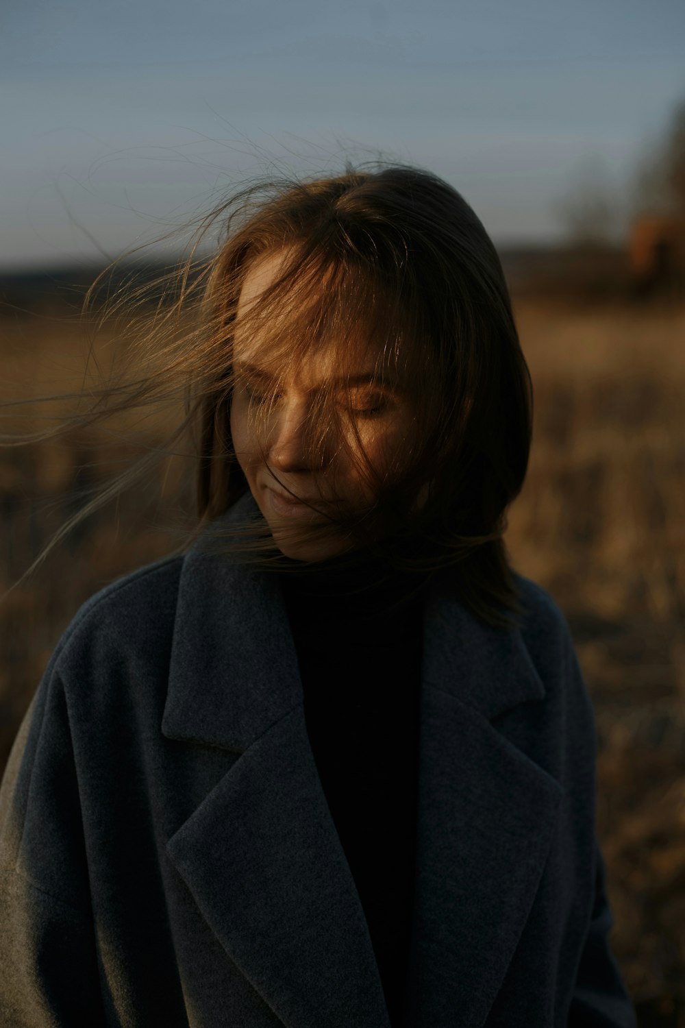 femme en manteau gris debout sur le champ brun pendant la journée
