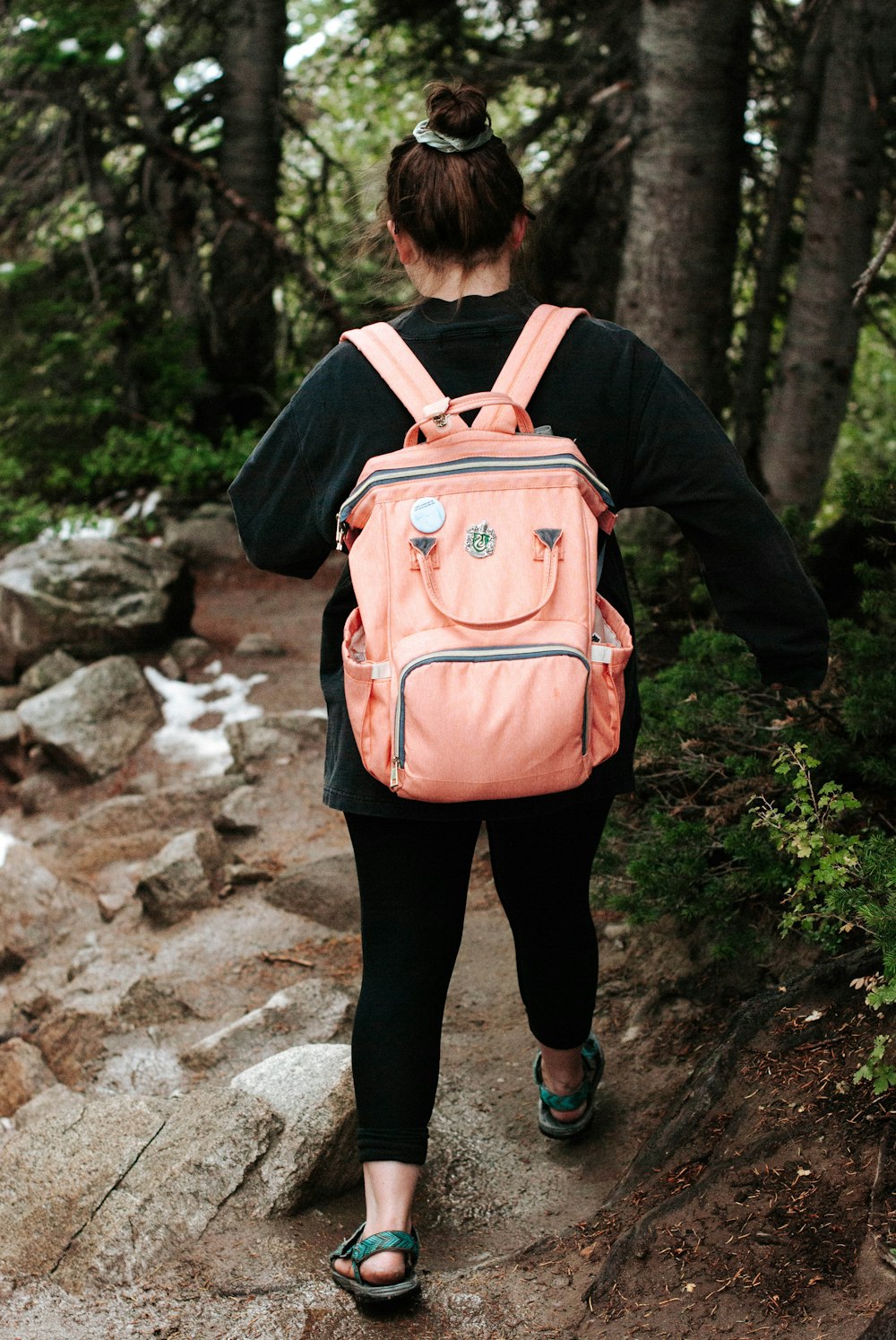 woman in black jacket with red backpack standing on rocky ground