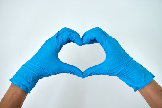 a pair of hands wearing blue latex gloves touching together to form a love shape