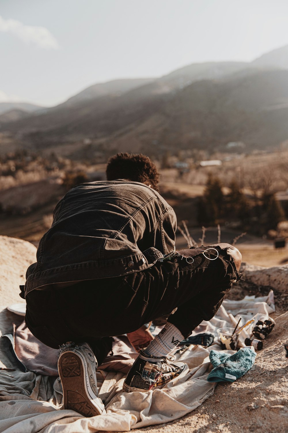 man in black jacket and black pants sitting on brown rock during daytime