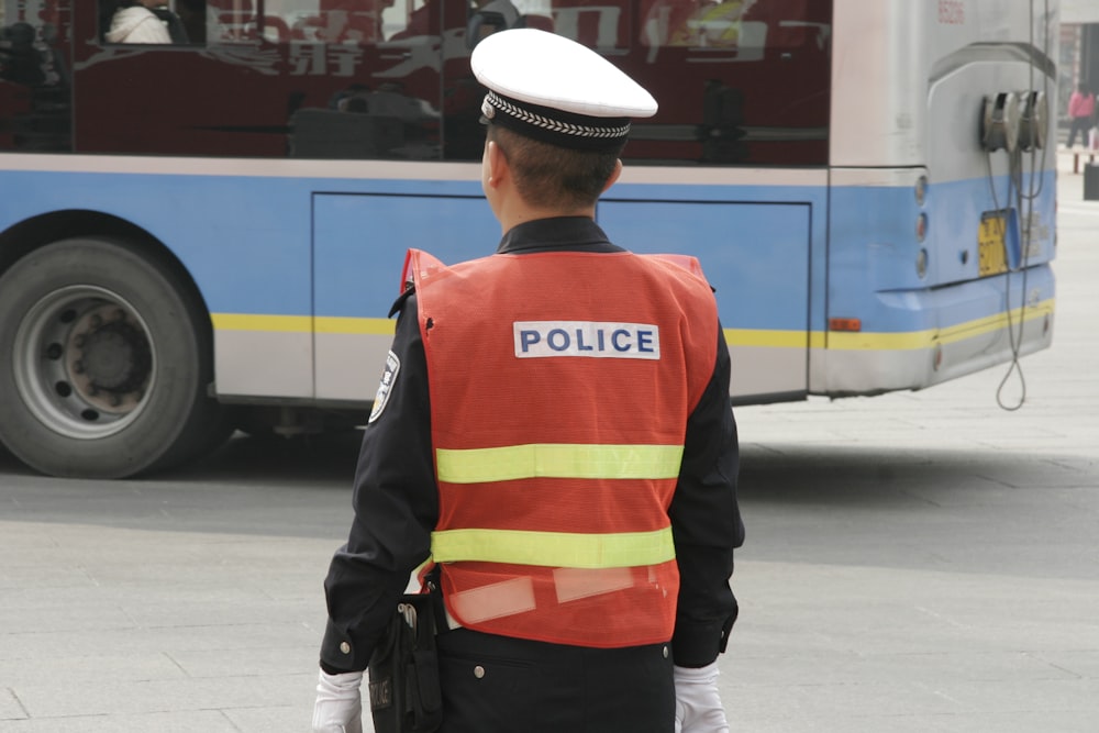 man in orange and black jacket wearing white hat standing on sidewalk during daytime