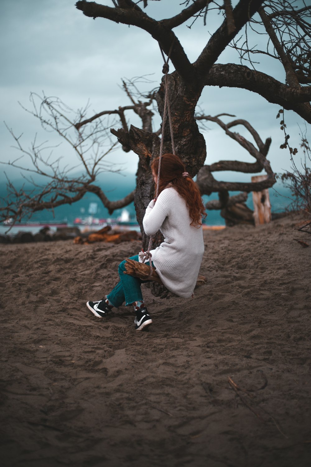 Femme en chemise blanche à manches longues et jean en denim bleu assise sur une branche d’arbre pendant la journée