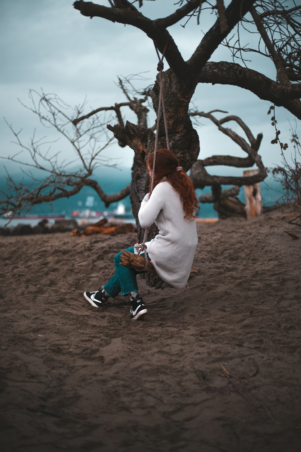 woman in white long sleeve shirt and blue denim jeans sitting on tree branch during daytime