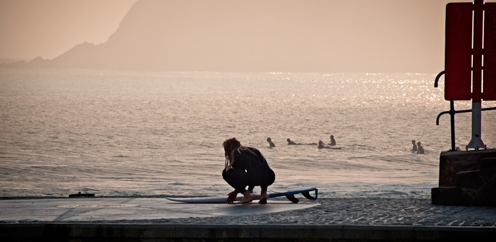 woman in black jacket sitting on blue surfboard on beach during sunset