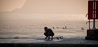 woman in black jacket sitting on blue surfboard on beach during sunset