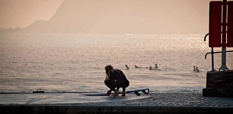 woman in black jacket sitting on blue surfboard on beach during sunset
