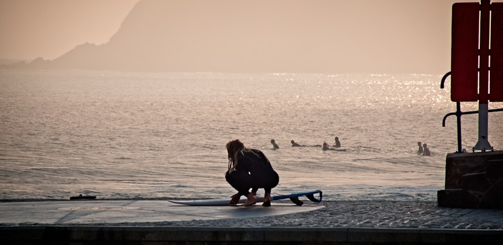 일몰 동안 해변에서 파란색 서핑 보드에 앉아 검은 재킷을 입은 여자