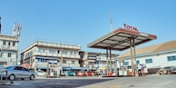 Wide shot of a bustling petrol station with vehicles fueling up, under clear skies.