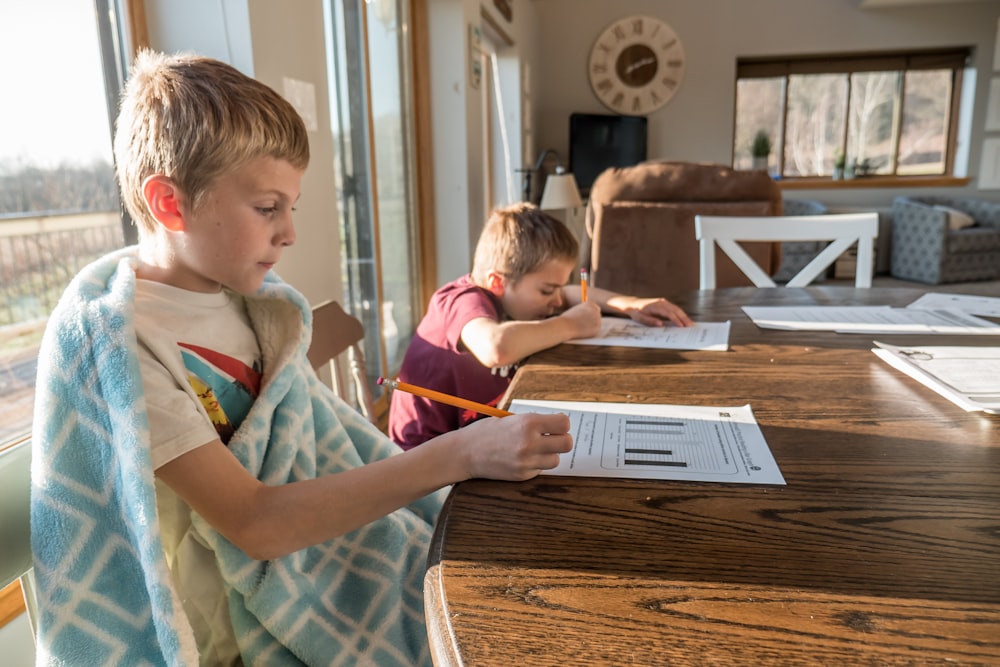 boy in white green and blue plaid button up shirt writing on white paper