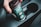 A hand is placing a brown and teal coffee cup into a car cup holder. The cup features a label that highlights ethically sourced ingredients.