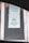 A printed notice taped to a window, indicating a preference for debit or credit card payments over cash. The sign includes a graphic of a hand holding a card. Another message is posted above, possibly policy or informational text.