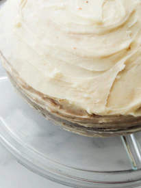 Close-up of a slice of homemade cake with soft caramel layers and creamy frosting on a ceramic plate.
