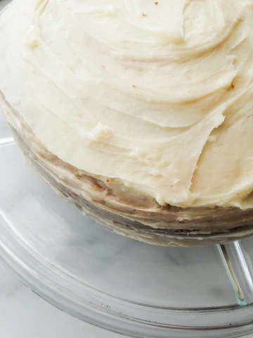 Close-up of a slice of homemade cake with soft caramel layers and creamy frosting on a ceramic plate.