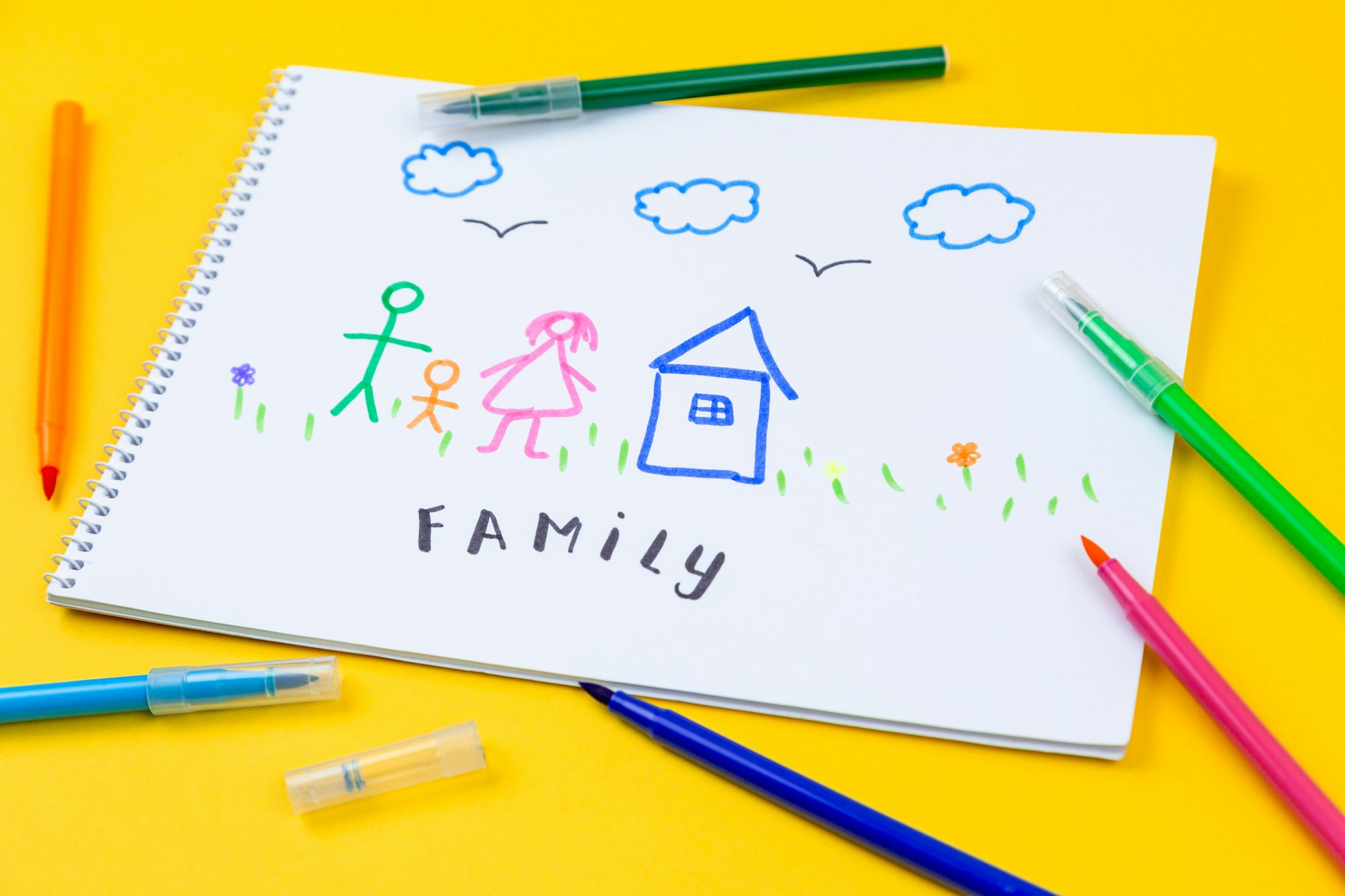 Stick drawing of a family and their house on paper using rainbow-colored pens.