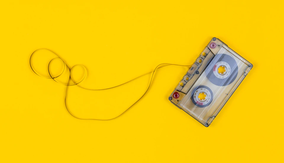 Vintage cassette tape rests on yellow background, coiled up neatly with two sides facing upwards