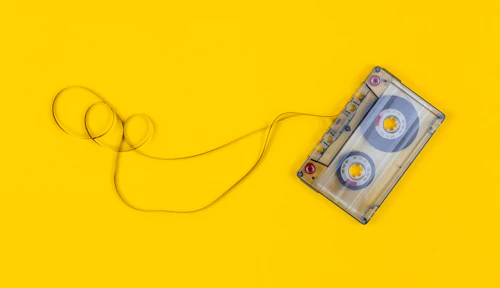 A clear cassette tape with its ribbon pulled loose on yellow