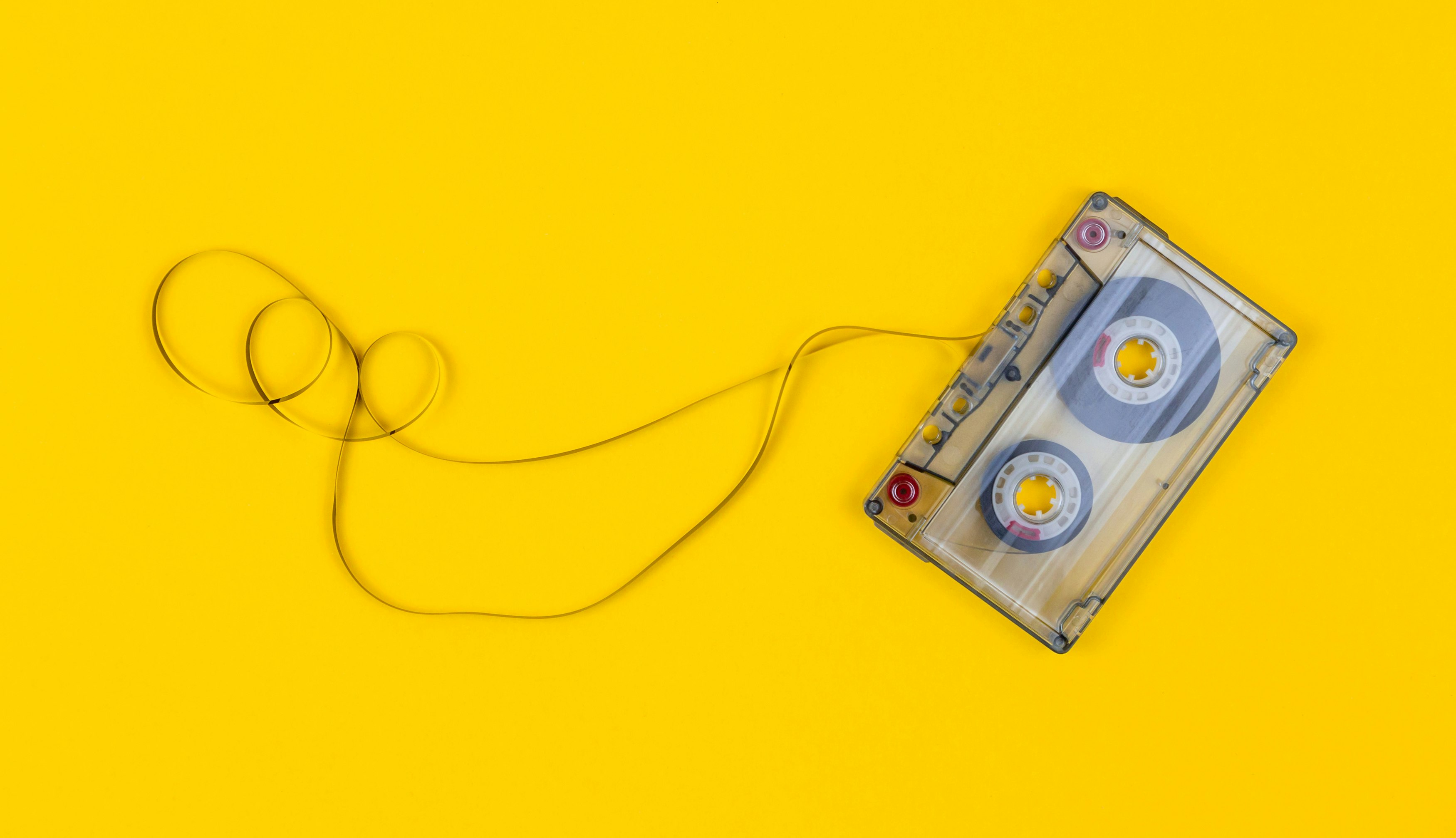 Top view of audio cassette with tangled tape on bright yellow background with copy space, minimalistic composition