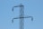 A section of a high-voltage power line tower is depicted against a clear blue sky. The steel structure is seen with two insulators attached on either side, and wires dangle from the insulators.