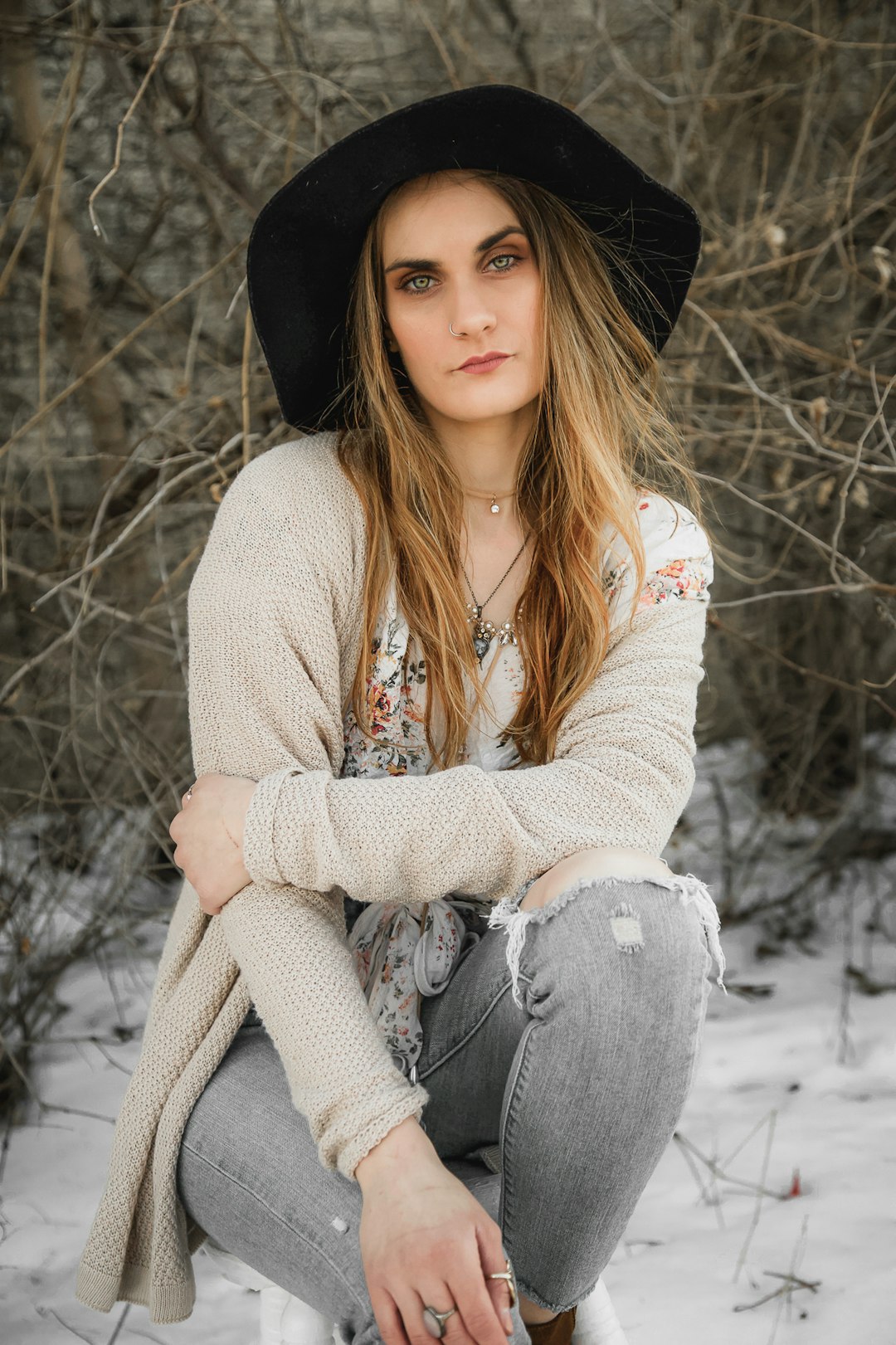 woman in white knit sweater and blue denim jeans sitting on snow covered ground during daytime
