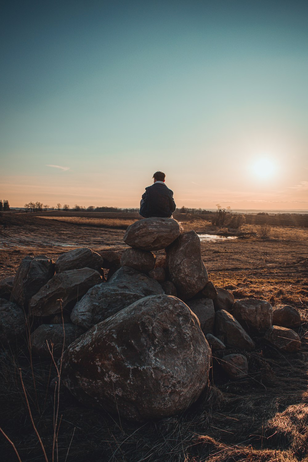 man sitting on rock formation during sunset