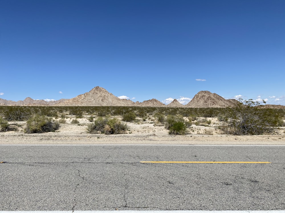 gray asphalt road near brown mountain under blue sky during daytime