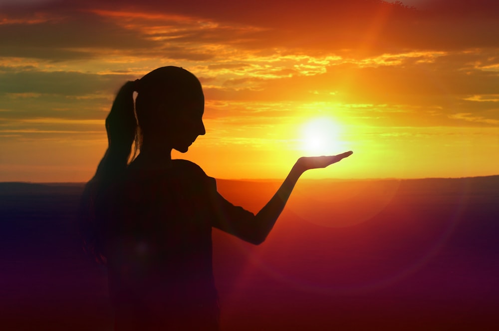 Silhouette einer Frau, die während des Sonnenuntergangs ihre rechte Hand hebt