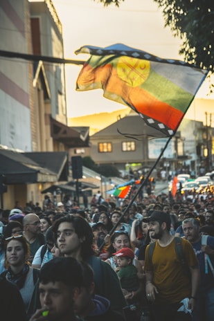 A vibrant crowd waving orange flags during a lively street rally at sunset.