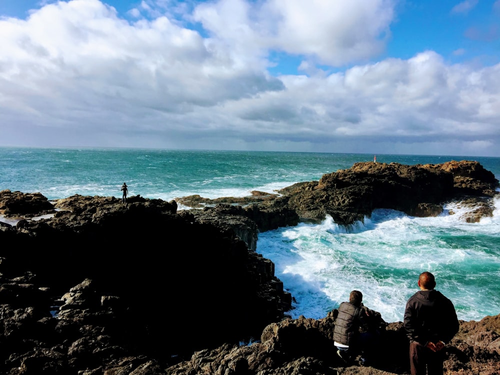 people sitting on rock formation near sea under blue and white cloudy sky during daytime