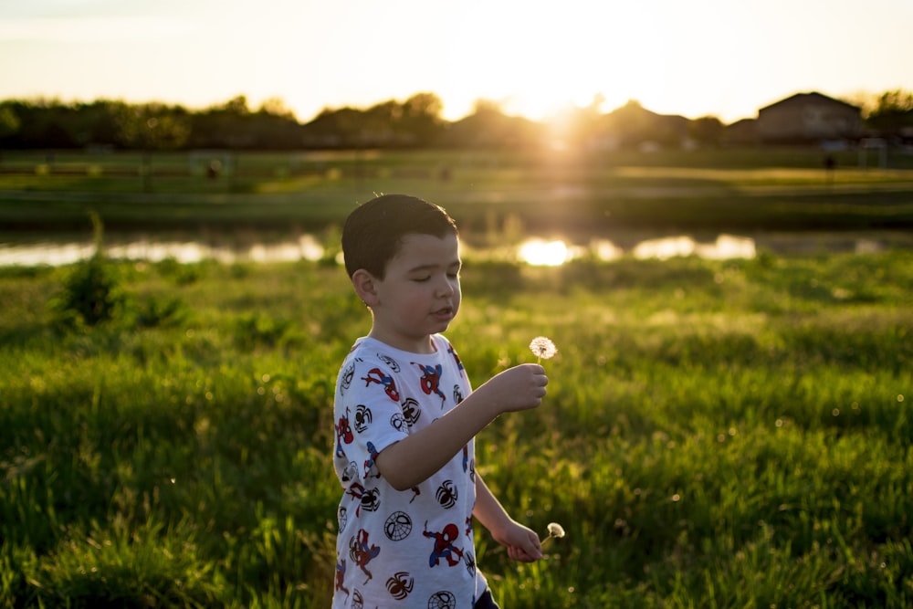 girl in white and blue floral dress standing on green grass field during sunset