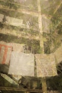 A multi-story residential building with lush greenery and plants on the balconies. Laundry is hung out to dry, including large sheets and possibly blankets. The structure appears to be aged with visible concrete, and the atmosphere is peaceful with a sense of everyday life.