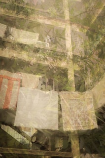 A multi-story residential building with lush greenery and plants on the balconies. Laundry is hung out to dry, including large sheets and possibly blankets. The structure appears to be aged with visible concrete, and the atmosphere is peaceful with a sense of everyday life.