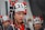A child wearing a traditional outfit adorned with intricate beads and decorations stands prominently. The headpiece features black fabric with white beads, silver ornaments, and red accents. In the background, more children are wearing similar attire, slightly out of focus.
