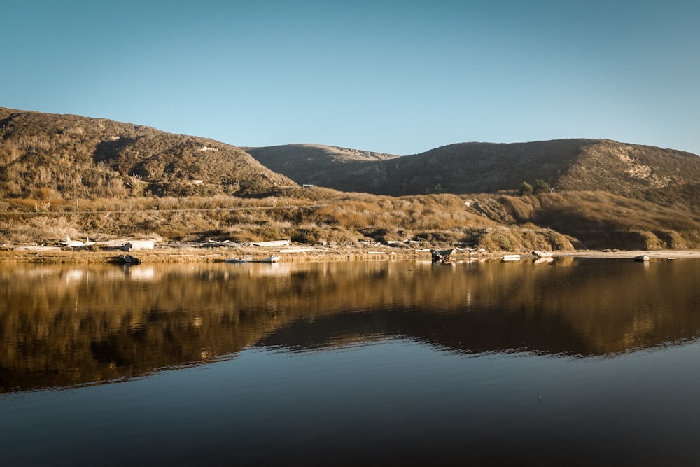 brown and green mountains beside lake under blue sky during daytime