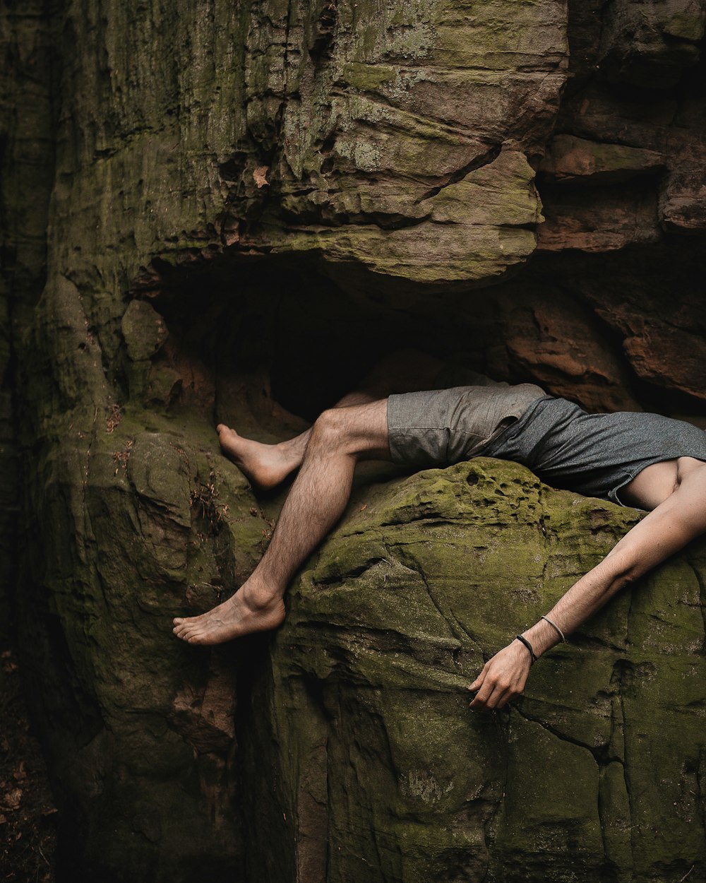 man in gray t-shirt and gray shorts lying on brown rock