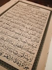 An open book with text written in Arabic script, featuring ornate calligraphy. The page is framed by an elaborate border and the content is aligned in clear rows across the page.