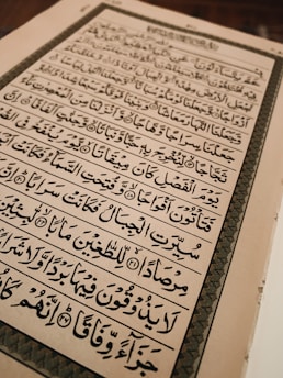 An open book with text written in Arabic script, featuring ornate calligraphy. The page is framed by an elaborate border and the content is aligned in clear rows across the page.
