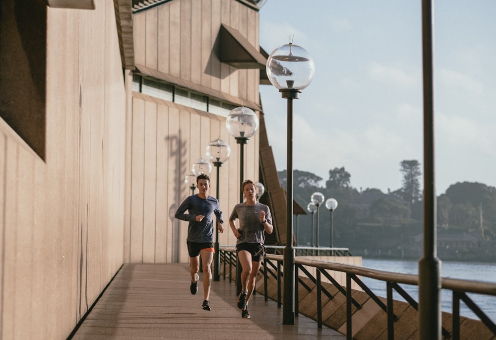 man in black t-shirt and blue shorts running on brown wooden dock during daytime