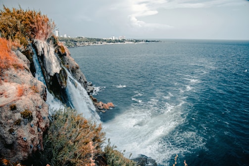 body of water near mountain under white clouds during daytime