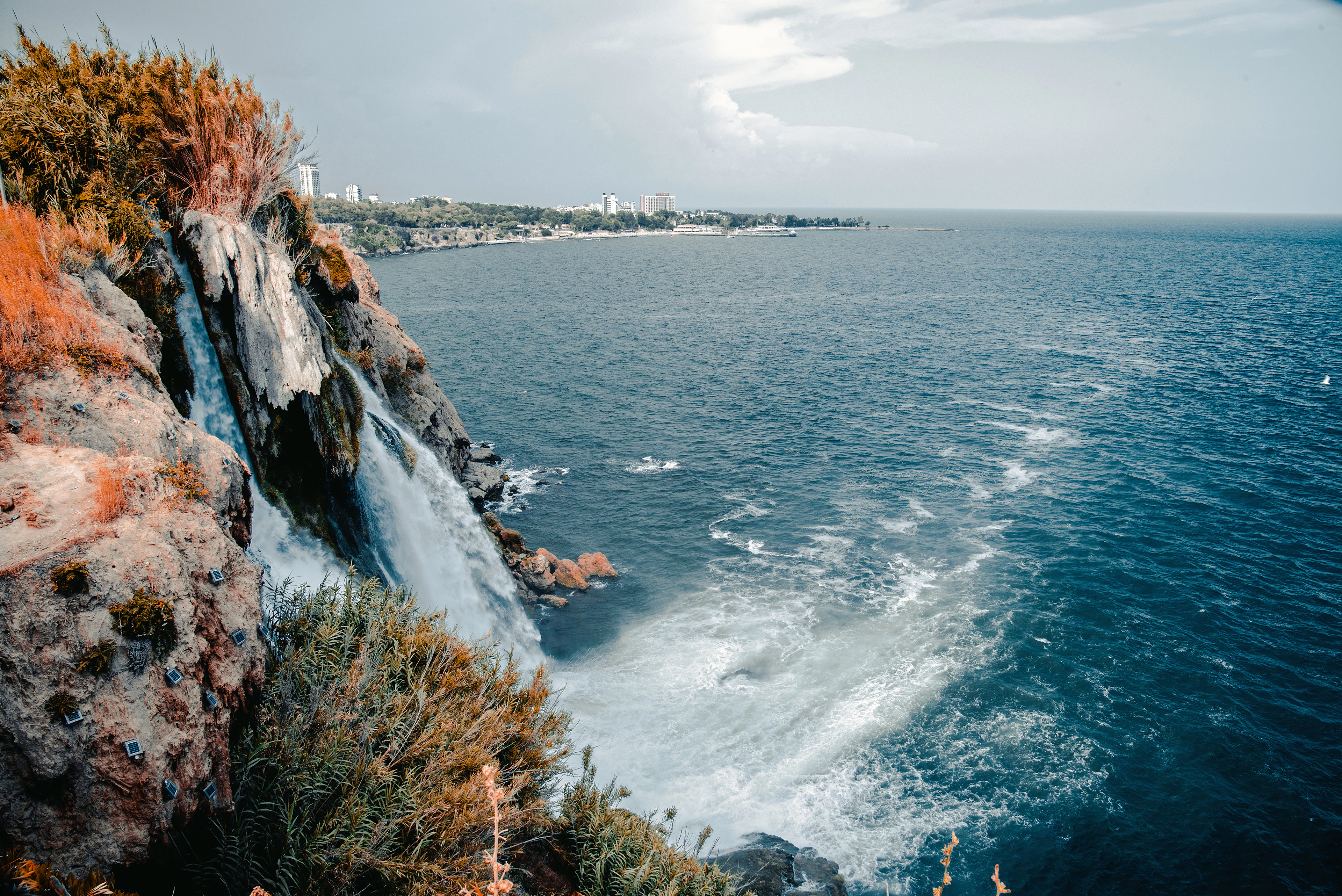 The Lower Duden waterfall dropping straight off the cliff into the Mediterranean at Antalya, the city's coastline curving away behind