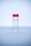 A clear test tube with a red cap and a label that reads '2019-NCOV' is placed upright against a light blue background. The tube is primarily filled with a clear liquid.