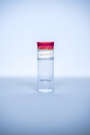 A clear test tube with a red cap and a label that reads '2019-NCOV' is placed upright against a light blue background. The tube is primarily filled with a clear liquid.
