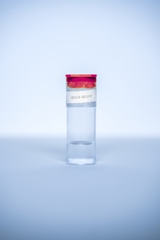 A clear test tube with a red cap and a label that reads '2019-NCOV' is placed upright against a light blue background. The tube is primarily filled with a clear liquid.